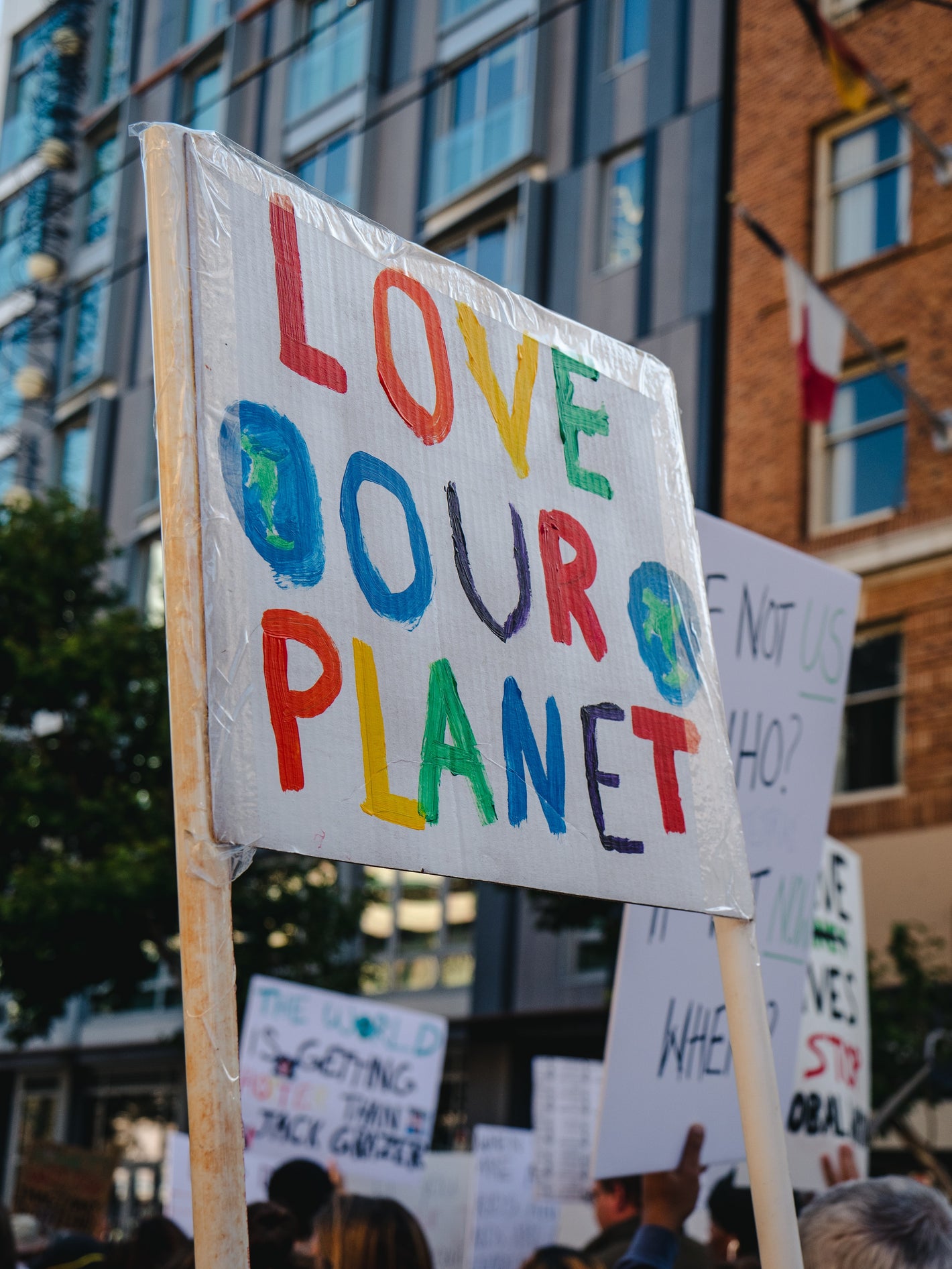 An environmental protest held in a city, with protesters holding up a large sign which reads "LOVE OUR PLANET".  